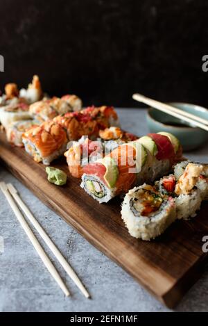 Nahaufnahme von verschiedenen Sushi-Rollen auf Holztablett mit schwarzem Hintergrund. Stockfoto