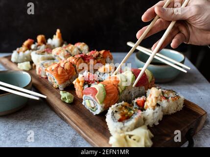 Hand mit Essstäbchen, um eine Sushi-Rolle von einer Platte. Stockfoto