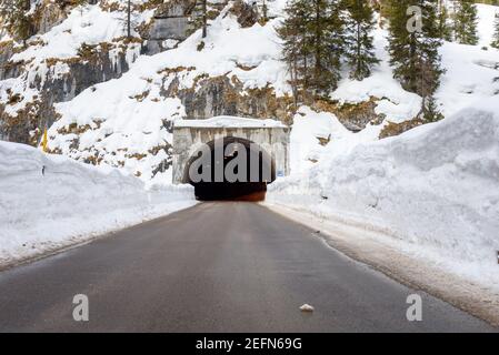 Eingang eines Tunnels entlang einer Bergstraße, die dazwischen verläuft Wände aus gepflügten Schnee im Winter Stockfoto