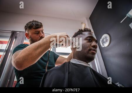 Ein junger afrikanischer Junge bekommt von ihm die Haare geschnitten Friseur Stockfoto