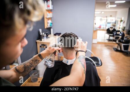 Barber benäht die Haare des Kunden mit einem Spray und kämmt es dann. Stockfoto
