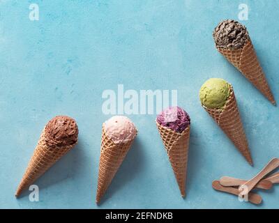 Verschiedene Eis Schaufeln in Kegel mit kopieren. Bunte Eis in der Waffel mit Schokolade, Erdbeere, Heidelbeere, Pistazien oder Matcha, Kekse, Schokolade, Sandwich Cookies auf blauem Hintergrund. Ansicht von oben Stockfoto