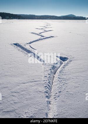 Frisches Pulver auf dem gefrorenen See mit Spuren von Eisläufern. Im Hintergrund die frostigen Wälder Stockfoto