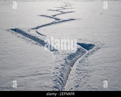 Der helle Schnee die Spuren des Eislaufens auf dem Eis. Gefrorener Bergsee bedeckt Schnee und Eisläufer machen schöne geschwungene Linien hinter Schlittschuhe. Stockfoto