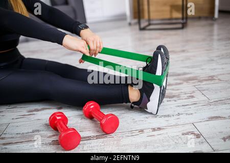 Lächelnde junge Frau beim Training mit Gummiband zu Hause Fitness-Workout. Gesundes Lifestyle-Konzept. Sport zu Hause während der Quarantäne Stockfoto