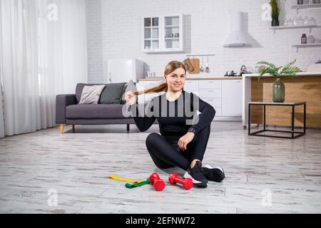 Lächelnde junge Frau beim Training mit Gummiband zu Hause Fitness-Workout. Gesundes Lifestyle-Konzept. Sport zu Hause während der Quarantäne Stockfoto