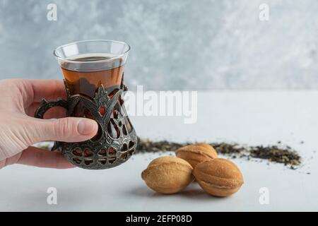 Weibliche Hand hält eine Tasse Kräutertee mit süßen Nußbaum geformter Keks Stockfoto