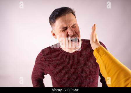 Crop Person Slapping verängstigten Mann im Gesicht. Emotional männlich immer ins Gesicht geschlagen, während schreien mit geschlossenen Augen in Angst auf weißem Hintergrund. Stockfoto