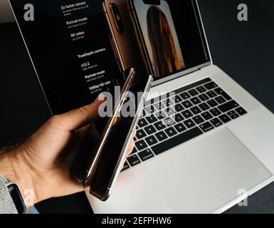 Paris, Frankreich - Sep 25, 2018: POV männliche Hand halten vergleichen, wie dünn die beiden neuen neuesten Smartphones von Apple Computers iPhone 11 12 14 Pro gegen die Pro max Versionen - mit MacBook Pro Laptop im Hintergrund Stockfoto