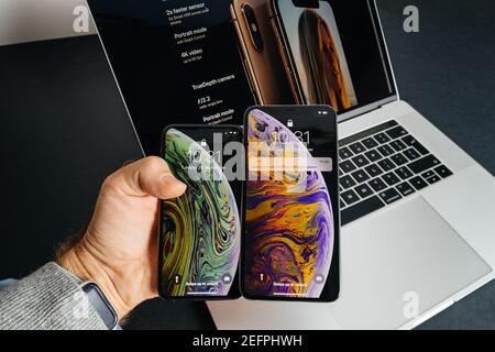 Paris, Frankreich - 25. Sep 2018: POV männliche Hand hält vergleichen zwei neue neueste Smartphones von Apple Computers iPhone 11 12 14 Pro gegen die Pro max Versionen - mit MacBook Pro Laptop im Hintergrund Stockfoto