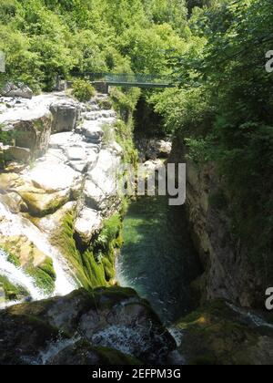 Vertikale Aufnahme einer Brücke über den Fluss inmitten der Felsen umgeben von grünen Bäumen Stockfoto