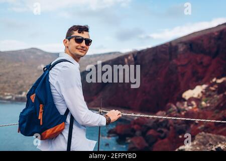 Touristen genießen Red Beach, Ägäis Meer und Berglandschaft aus Sicht Punkt in Akrotiri, Santorini Insel, Griechenland. Glücklicher Mann Rucksacktourist unterwegs Stockfoto