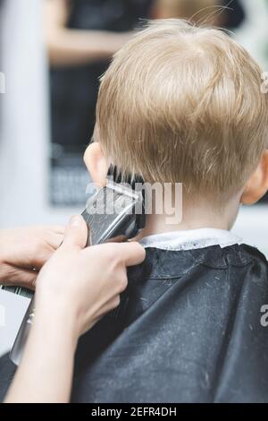 Friseur in Friseursalon Maschine Clipper Trimmer schneidet Haare Kind Junge. Nahaufnahme des Lebensstils. Konzept der Schönheit, Hygiene und. Rückansicht. Vertikale Aufnahme von Stockfoto