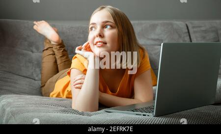 Nachdenkliche kaukasische schöne Frau liegt auf dem Sofa mit Laptop. Portrait von verträumten Teenager Mädchen denken hinter Laptop zu Hause im Wohnzimmer mit crosse Stockfoto