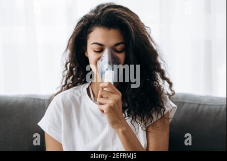 Nahaufnahme einer kranken afroamerikanischen Frau mit Inhalator. Ungesunde Millennial Mädchen tun Inhalation zu Hause, sie verwenden Vernebler und Inhalator für die Behandlung. Husten und Grippe Stockfoto