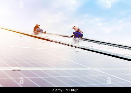 Elektroingenieure mans arbeiten daran, Sonnenkollektoren auf Solarstation auf dem Dach gegen blauen Himmel bei Sonnenuntergang zu installieren. Entwicklung Sonne alternative Energie Stockfoto