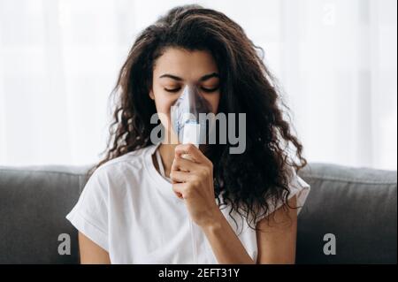 Nahaufnahme einer kranken afroamerikanischen Frau mit Inhalator. Ungesunde Millennial Mädchen tun Inhalation zu Hause, sie verwenden Vernebler und Inhalator für die Behandlung. Husten und Grippe Stockfoto