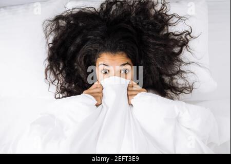 Lächelnd multirassische schwarze lockige Mädchen nutzt Handy, im Gespräch mit Freunden oder Familie, während sitzt auf der Couch im Wohnzimmer und schaut auf Kamera, Kommunikationskonzept Stockfoto