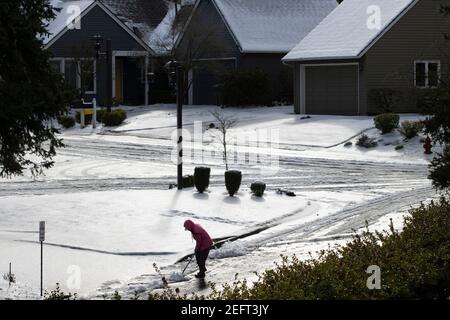 Eine Frau schaufelt am 15. Februar 2021 nach Schnee und eiskalten Regen auf einer Straße in der Nachbarschaft des Lake Oswego, Oregon, Schnee und Eis. Stockfoto