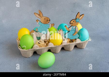 Mehrfarbige ostereier mit osterhasen im Eierkarton auf Grauer Hintergrund Stockfoto