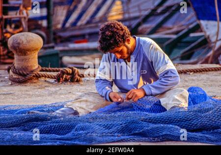 Junger Mann, der Fischernetze im Hafen von Agadir, Marokko, ausbessern kann. Stockfoto