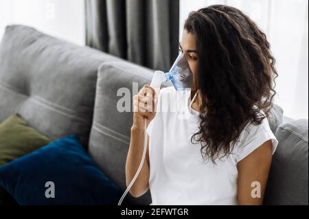 Nahaufnahme einer kranken afroamerikanischen Frau mit Inhalator. Ungesunde Millennial Mädchen Inhalation zu Hause, sie verwenden Vernebler und Inhalator für die Behandlung sitzen auf der Couch zu Hause in quara Stockfoto