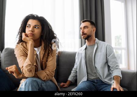 Multirassische Paar in der Liebe streiten zu Hause auf der Couch über Haushalt oder finanzielle Probleme. Die Frau wird vom Mann beleidigt und ignoriert ihn. Häusliche Familie Konflikte Konzept Stockfoto