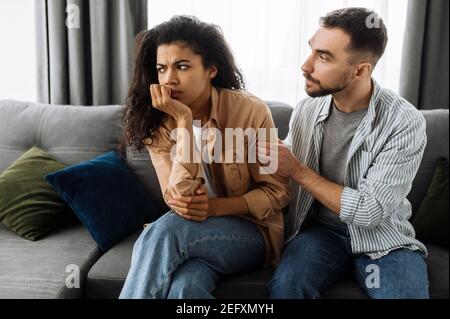 Multirassische Paar in der Liebe streiten zu Hause auf der Couch über Haushalt oder finanzielle Probleme. Die Frau wird vom Mann beleidigt und ignoriert ihn. Häusliche Familie Konflikte Konzept Stockfoto
