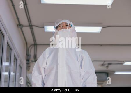 Müde junge medizinische Mitarbeiter tragen PSA-Anzug mit schützendem Gesicht Schild und Maske arbeiten im Krankenhaus während Covid-19 Pandemie Stockfoto