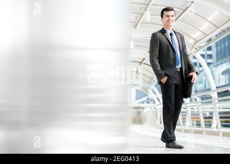 Lächelnder junger Geschäftsmann, der eine Tasche trägt, während er im überdachten Gang im Freien läuft, voller Körper Stockfoto