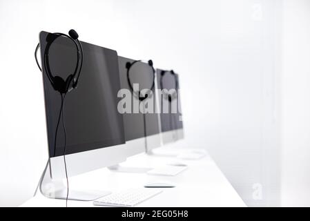 Mikrofon-Headsets hängen an Computermonitoren im Callcenter Stockfoto