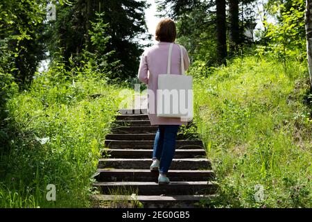 Frau in rosa Jacke mit leeren wiederverwendbaren Einkaufstasche Mockup. Weibliche Hand halten Leinwand umweltfreundliche Tasche Nachbau Stockfoto