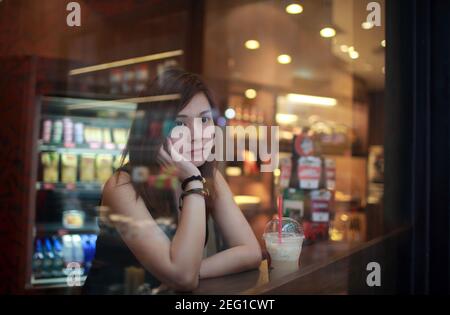 Junge Mädchen warten jemand, der spät, Hand auf Kinn, und Blick hinter das Café-Fenster, Moment der genießen Sie ihre Tee Zeit tief Denken in hongkong Stockfoto