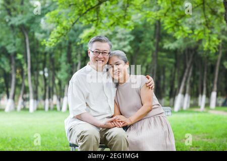Glückliches altes Paar, das auf Stühlen in den Parkarmen sitzt Um die Schultern