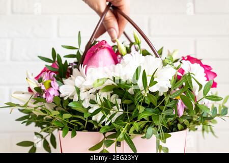 Frau Floristin macht eine schöne Blumenkomposition in einem Blumenladen. Frühlingsbouquet in rosa Box mit Griffen. Stockfoto