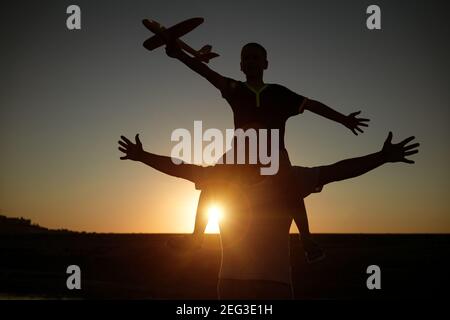 Papa hält seinen Sohn bei Sonnenuntergang um den Hals Im Sommer starten sie ein Flugzeug vor dem Hintergrund Der Himmel Stockfoto