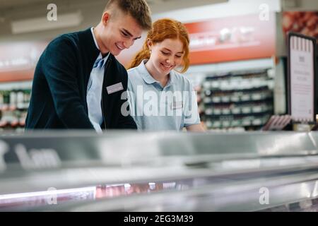 Arbeiterinnen und Arbeiterinnen arbeiten im Supermarkt zusammen. Trainee Mitarbeiter Wiederannahme von Produkten im Lebensmittelgeschäft. Stockfoto