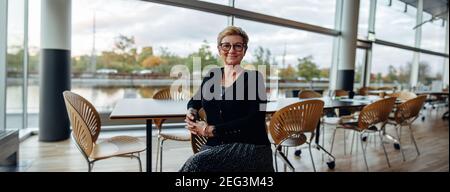 Ältere Frau, die in der Bürokantine sitzt. Reifer Business-Profi in hellen Büro. Stockfoto