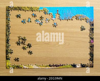Puzzle in den Anfangsphasen des Zusammenstellens auf einem Holztisch, während Covid-19 Lockdown. Stockfoto