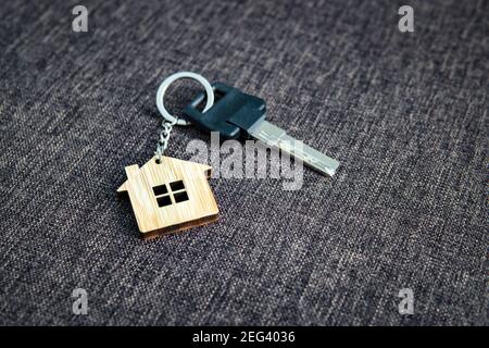 Nahaufnahme des Schlüssels mit dem hausförmigen Schlüsselring auf dunklem Sacktuch-Hintergrund. Konzept des Kaufens Wohnwohnung. Zu Hause sein. Der Hausschlüssel liegt auf dem Stockfoto
