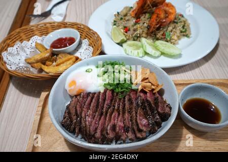 Wagyu Rindfleisch Reis serviert mit Rührbraten Garnelen Reis und Gebratener Kartoffelkeil Stockfoto