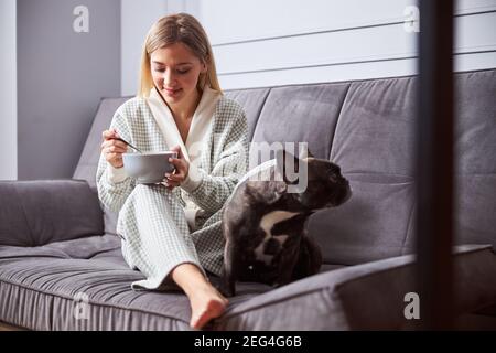 Weibchen mit einem Hund, der aus der Schüssel auf dem Sofa isst Stockfoto