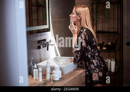 Frau, die ihr Gesicht in einem Badezimmerspiegel überprüft Stockfoto