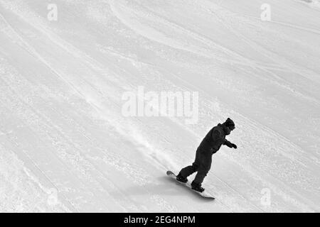 Snowboarder bergab auf der Skipiste am kalten Wintertag. Schwarzweißbild. Stockfoto