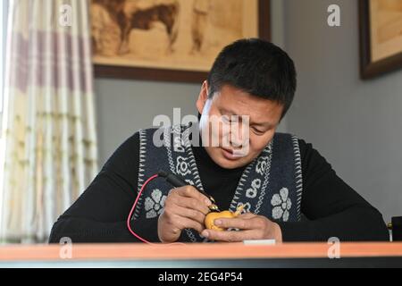 (210218) -- HORGOS, 18. Februar 2021 (Xinhua) -- Cao Guangyao arbeitet an pyrographischen Kalabash-Kunstwerken in seinem Atelier in Horgos, nordwestlich von Xinjiang Uygur Autonome Region, 6. Februar 2021. Cao Guangyao ist ein 45-jähriger Bauer in Horgos. Er ist auch bei den Einheimischen als Künstler für seine pyrographischen Kalabash-Kunstwerke bekannt. Als Maler-Enthusiast interessierte sich Cao vor 8 Jahren für pyrographische Kreation aus TV-Shows und begann seitdem seine eigene Kreation. Trotz keiner beruflichen Ausbildung, Cao machte Kunst Versuche immer wieder mit Liebe und Leidenschaft während der Lacksaison der Landwirtschaft Stockfoto