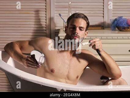 Junge attraktive Mann rasiert im Spiegel, Gay Rasieren im Bademantel im Badezimmer. Stockfoto
