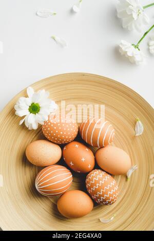 Ostereier im skandinavischen Stil in Teller und Frühlingsblumen auf weißem Hintergrund. Flache Lay-Komposition, Draufsicht. Einfacher nordischer Stil. Stockfoto