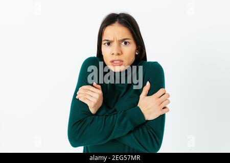 Junge Frau fühlt sich kalt und umarmt sich mit beiden Armen warm zu halten mit verärgerten Ausdruck auf weißem Studio Hintergrund. Stockfoto