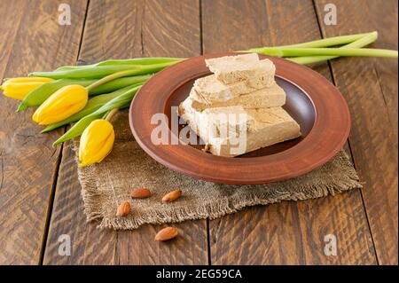 Teller mit Halva aus Sonnenblumenkernen und gelben Tulpen auf Holztisch. Stockfoto