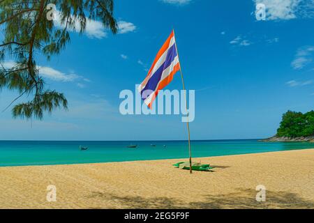 Ein tropischer Strand in Thailand mit der Nationalflagge flattert in der Meeresbrise, auf dem goldenen Sandstrand, mit einer Kulisse des azurblauen und klaren b Stockfoto